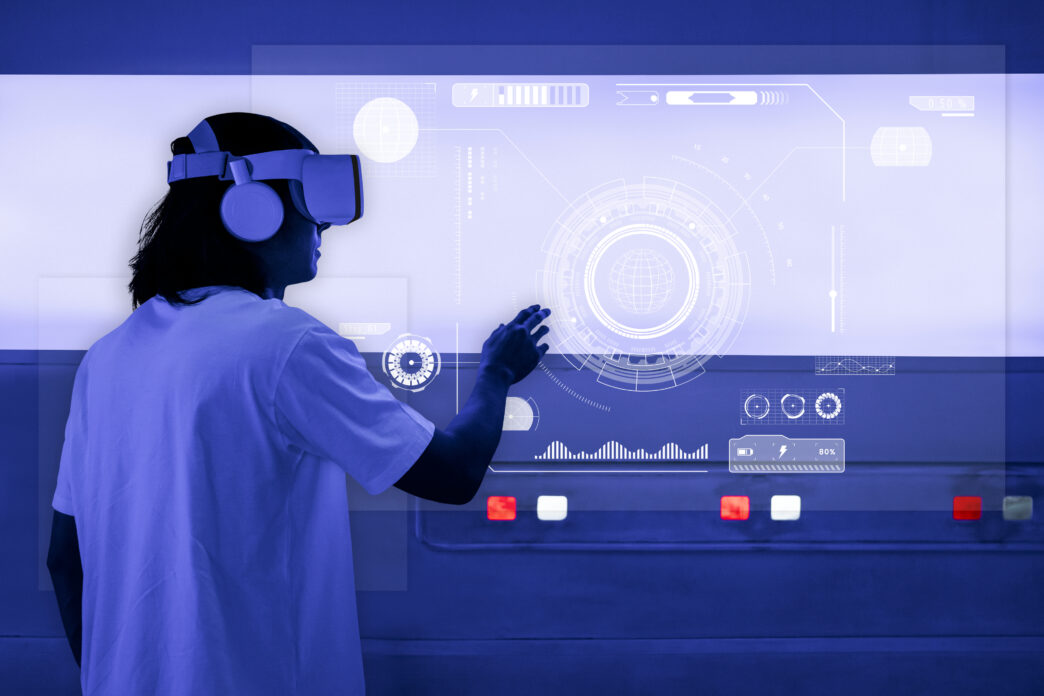 A person wearing a virtual reality headset and headphones, reaching out to interact with a futuristic, holographic interface in blue tones.