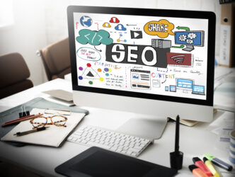 A computer monitor on a desk displaying an SEO concept sketch with colorful icons, text, and diagrams.