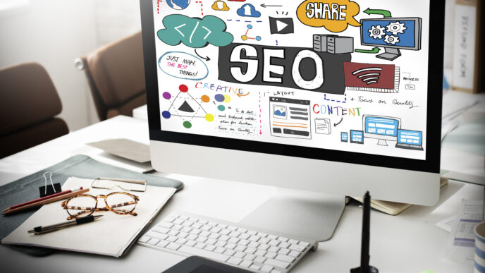 A computer monitor on a desk displaying an SEO concept sketch with colorful icons, text, and diagrams.